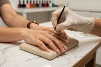 Application de pose américaine sur des ongles rongés par une technicienne en manucure dans un salon moderne